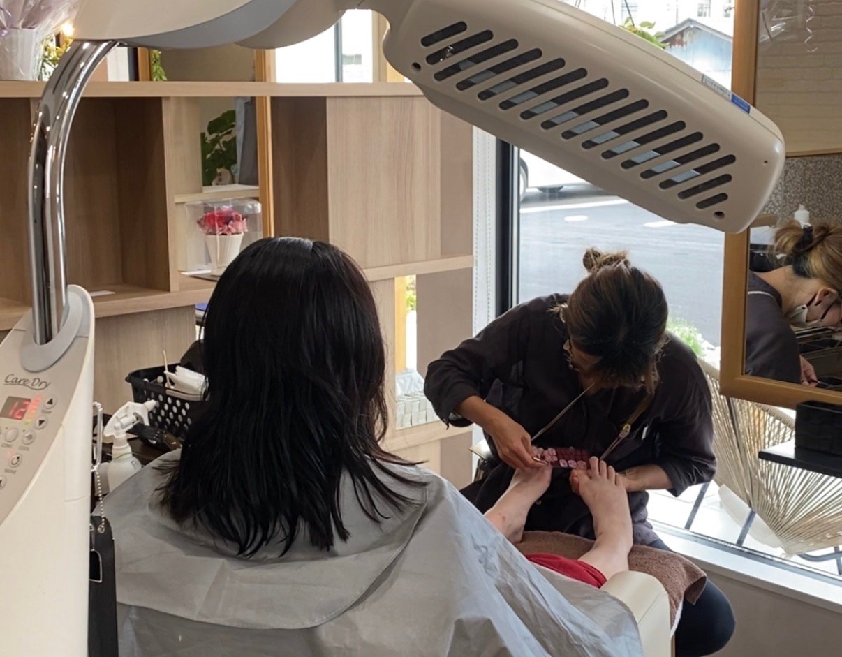 大きな窓のある明るい店内で、スタッフがお客様のフットケアを施術しているl’pur by shimaの様子