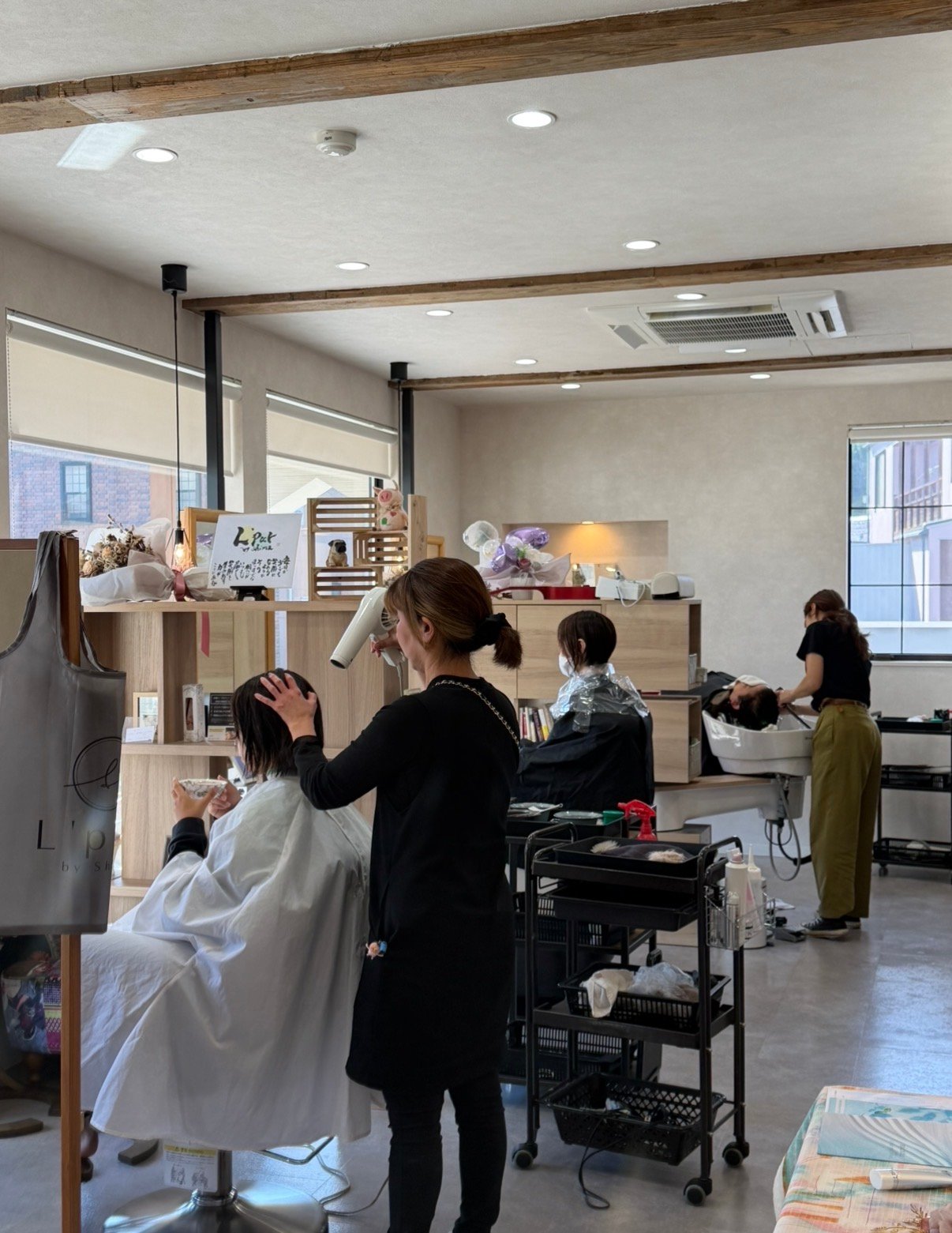 木の梁と大きな窓のある明るい店内で、スタッフがお客様の施術をしているl’pur by shimaの様子